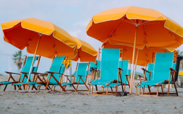 an image taken at the beach of a group of cyan blue chairs accompanied by bright yellow sun umbrellas