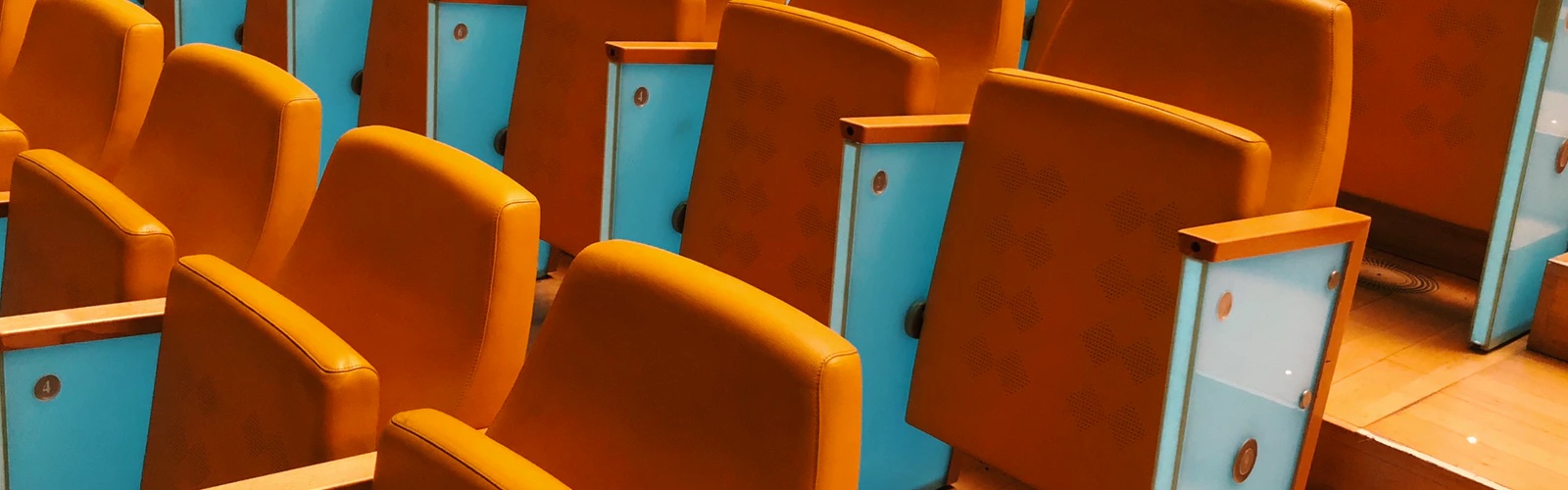 a close up landscape image of 2 rows of bright orange seats at a staduim with blue panels on the sides of the seats