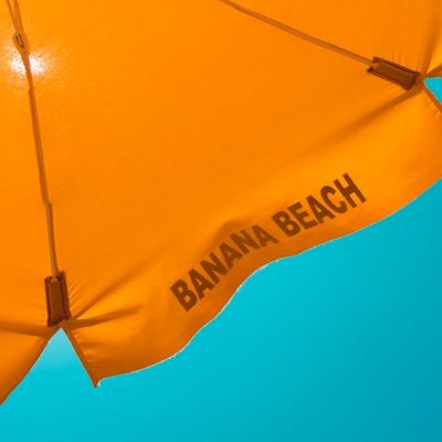 a close up image looking up and the top of an orange beach umbrella with the text 'banana beach'